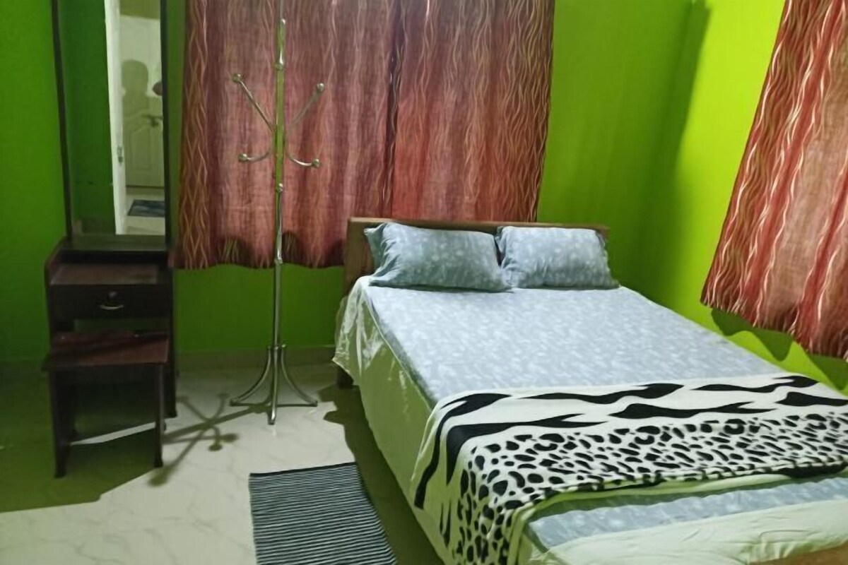 Een kamer met een bed, een klein houten tafeltje, een spiegel en een vloerlamp.