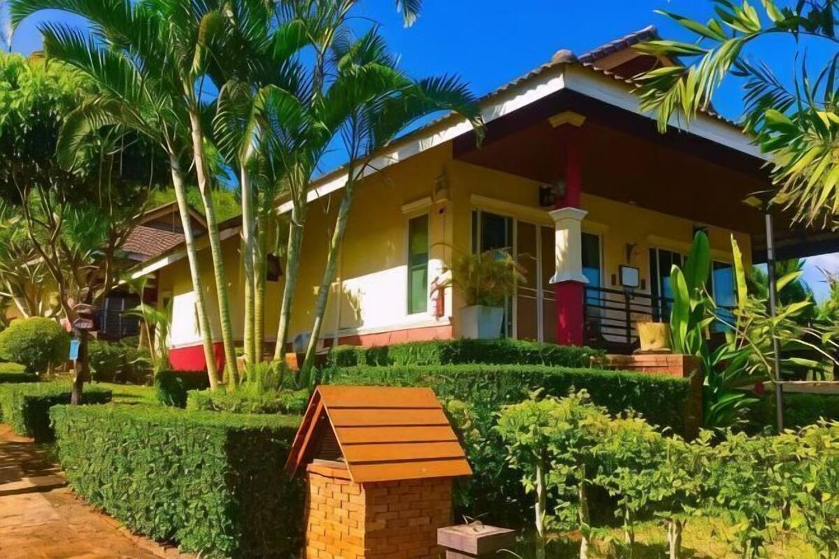 A two-story house with a porch, surrounded by well-maintained hedges and palm trees.