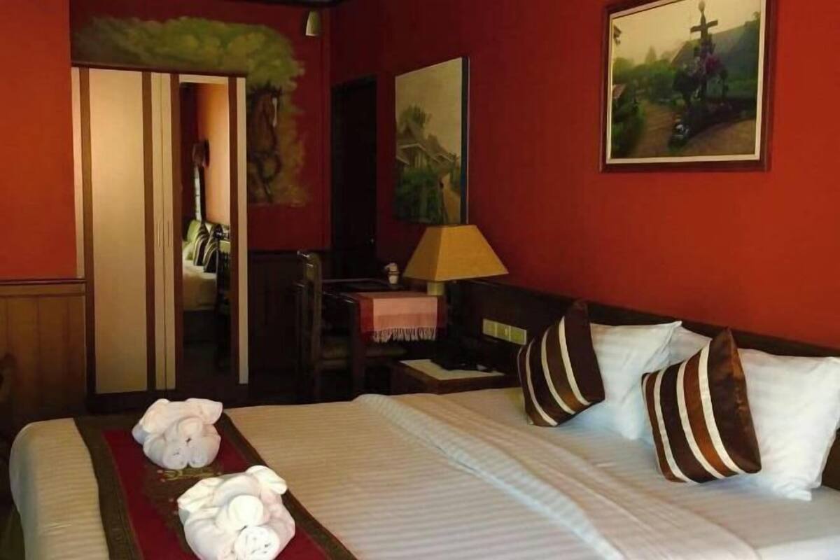A hotel room with a bed, pillows, a nightstand, a lamp, and a painting on the wall.