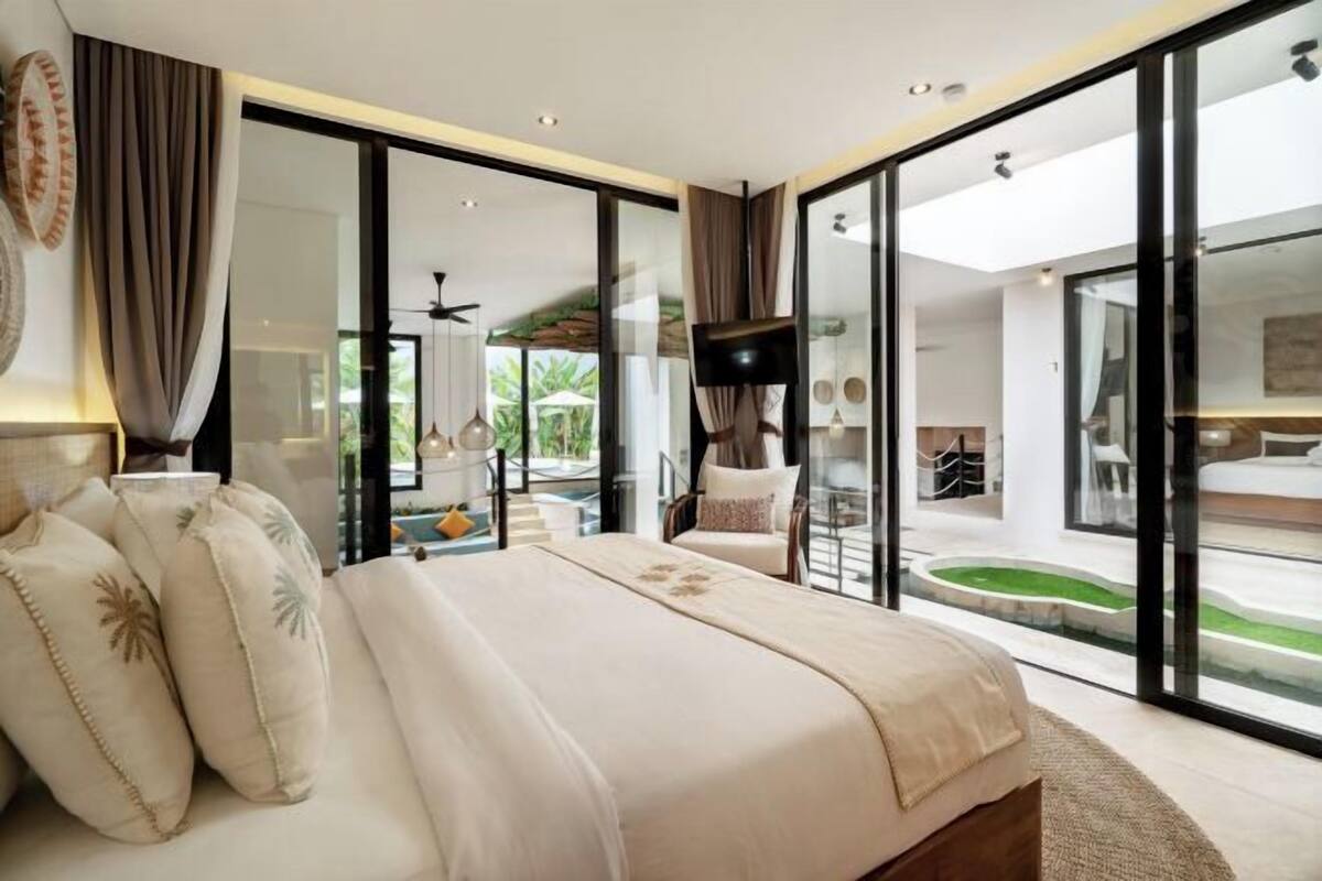 Ein modernes Schlafzimmer mit einem großen Bett, einem Fernseher und Blick auf einen Pool und eine Außenanlage.