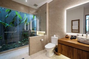 Een moderne badkamer met een glazen douchecabine, een wit toilet en een houten wastafelmeubel met een grote wasbak.