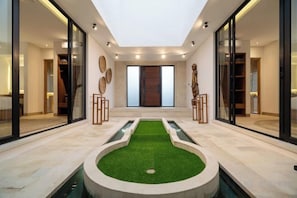 A modern interior with a central artificial green lawn, glass doors, and a view of a wooden door.