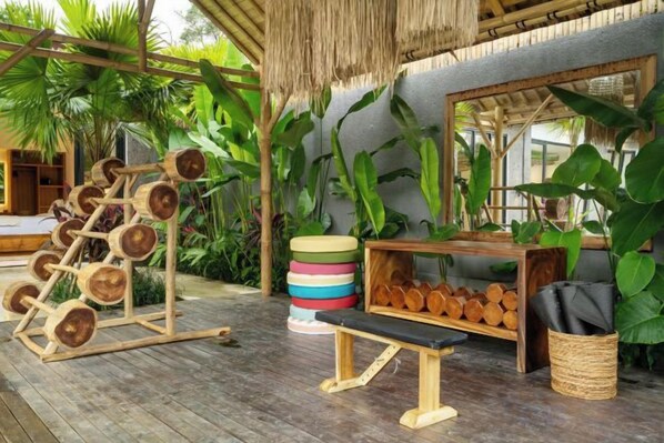 Una terraza de madera con una estación de levantamiento de pesas, un banco y un estante con troncos.