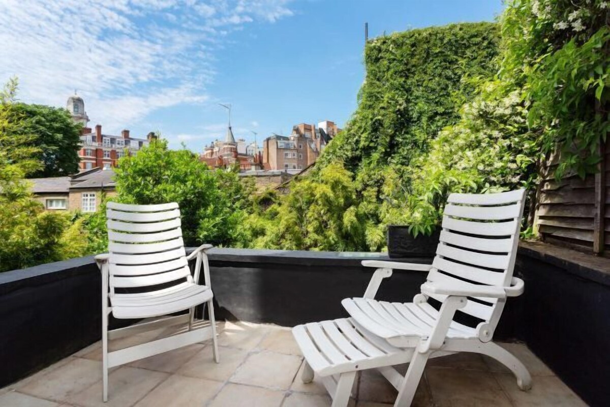 Two white lounge chairs on a balcony with a city view.