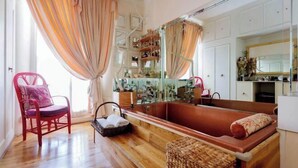 Una habitación con suelo de madera, una silla roja, un espejo grande y una bañera.