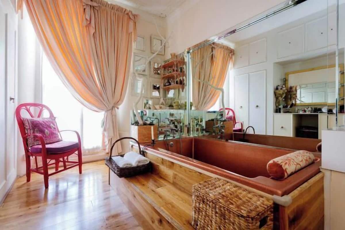 A room with a wooden floor, a red chair, a large mirror, and a bathtub.