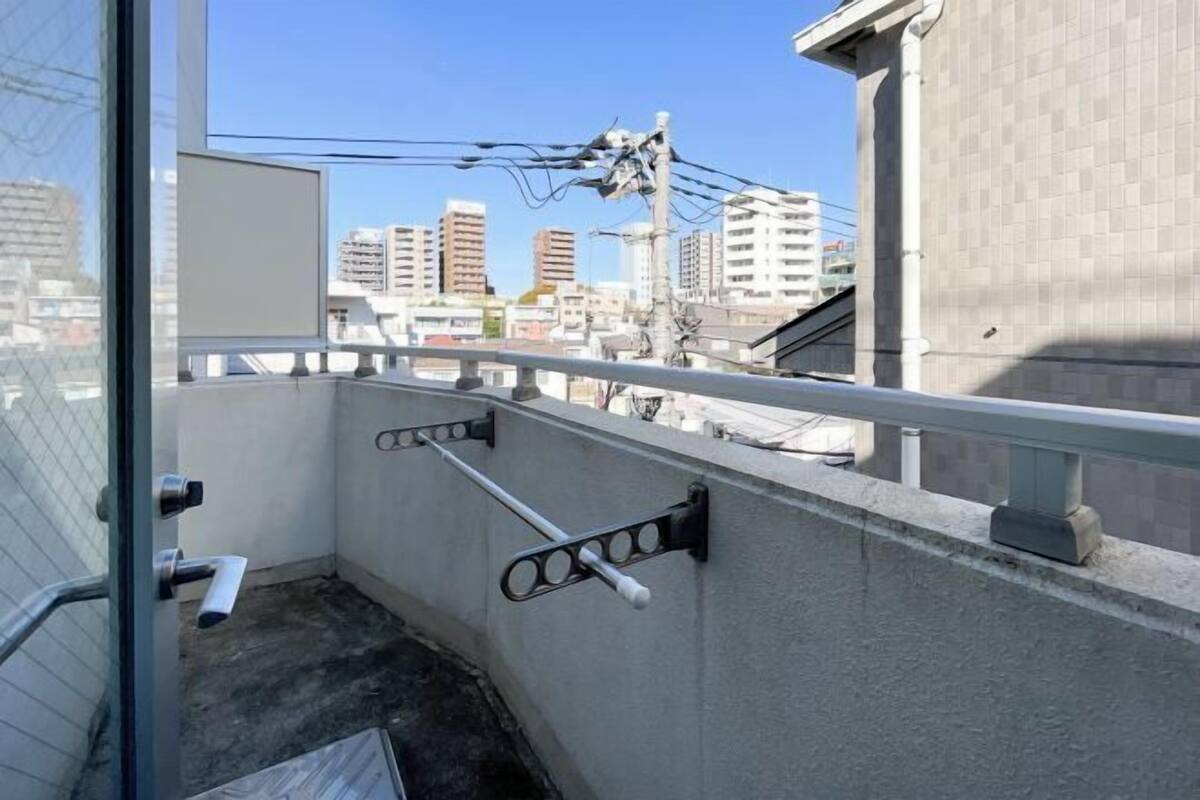 Un toit-terrasse avec une rambarde en métal, un mur en béton et une vue sur les bâtiments en arrière-plan.