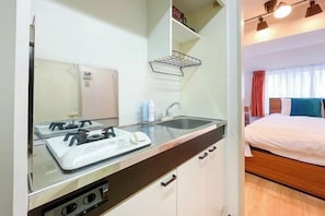 A compact kitchenette with a stove, sink, and cabinets, adjacent to a bed with a window view.