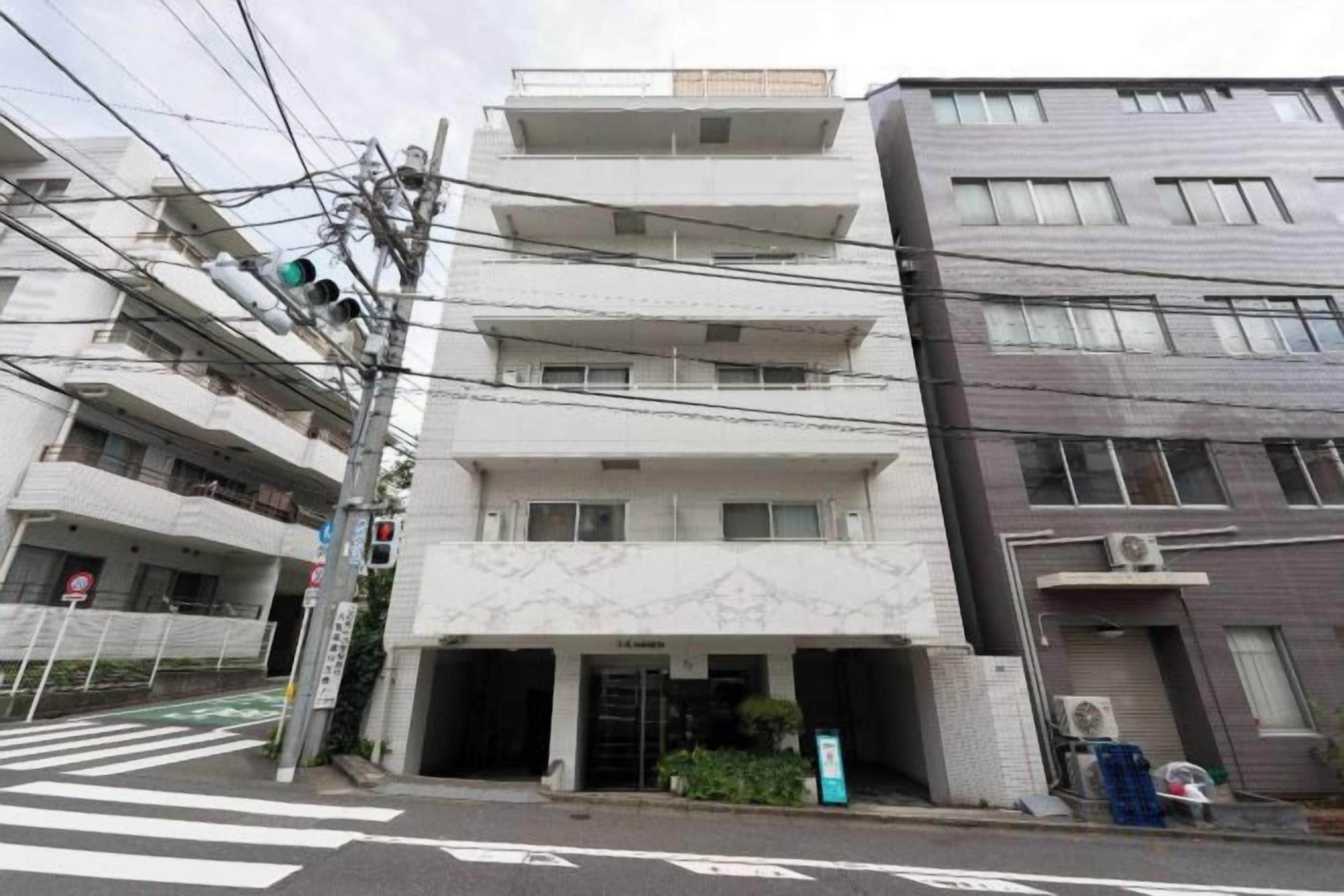 A multi-story building with a ground-level entrance, a visible balcony on the second floor, and a parking area in front.