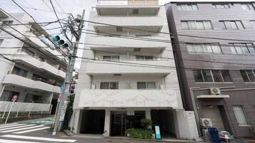 A multi-story building with a ground-level entrance, a visible balcony on the second floor, and a parking area in front.