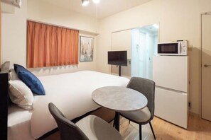 A hotel room with a bed, a small round table, two chairs, a TV, a microwave, and a door leading to another room.