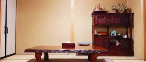 Una habitación japonesa tradicional con suelo de tatami, una mesa de madera baja, un televisor montado en la pared y un mueble de madera con objetos decorativos.