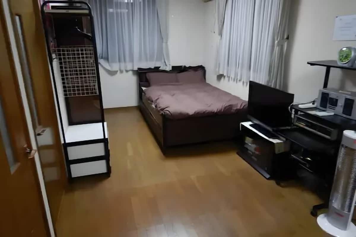 A bedroom with a bed, a desk with a computer, a heater, and a wardrobe.