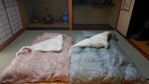 A traditional Japanese room with tatami flooring, a low table with a vase and a sunflower, and a bed with a pink and blue floral bedspread. - Private Villa Gifu Takayama (Takayama)