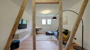 A loft-style room with exposed wooden beams, a black floor lamp, a sofa, and a TV mounted on the wall. - Stylish vacation apartment in Germany's highest train station (Feldberg (Schwarzwald))