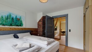 A neatly made bed with white linens and a gray throw blanket, a wooden headboard, a brick fireplace, and a painting of a forest on the wall. - Stylish vacation apartment in Germany's highest train station (Feldberg (Schwarzwald))