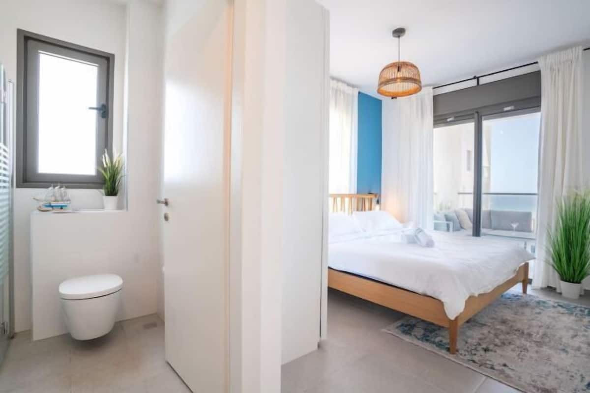 A bedroom with a bed, a window, a door, and a view of the outside.