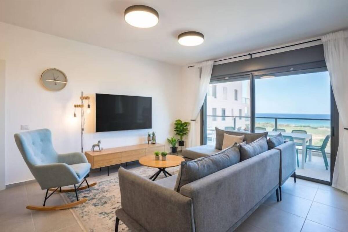 A modern living room with a sofa, a rocking chair, a TV, and a balcony with a view.
