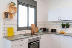 A modern kitchen with white cabinets, a built-in oven, and a window with blinds. - Stylish Seaside Escape with Balcony (Nahariyya)