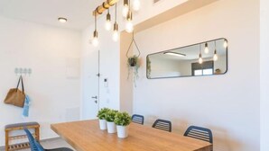 A dining area with a wooden table, black chairs, hanging lights, a mirror, and potted plants. - Stylish Seaside Escape with Balcony (Nahariyya)
