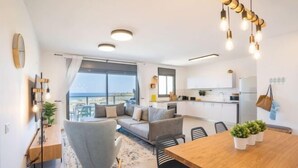 A modern apartment with a dining area, kitchen, and a large window offering a view. - Stylish Seaside Escape with Balcony (Nahariyya)
