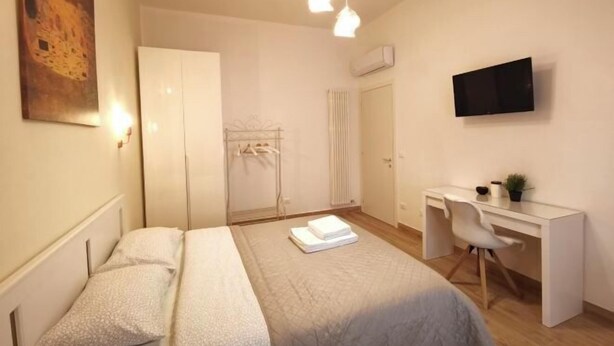 A modern bedroom with a bed, bedside table, desk, chair, and a mounted TV. - Casa di Serena (Venice)