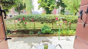 A patio area with a table and chairs, a potted plant, and a view of a garden with a fence and greenery. - Casa di Serena (Venice)