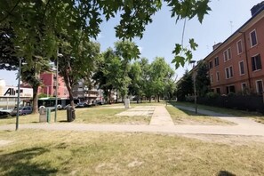 A park with grass, trees, a sidewalk, and a red building in the background. - Casa di Serena (Venice)