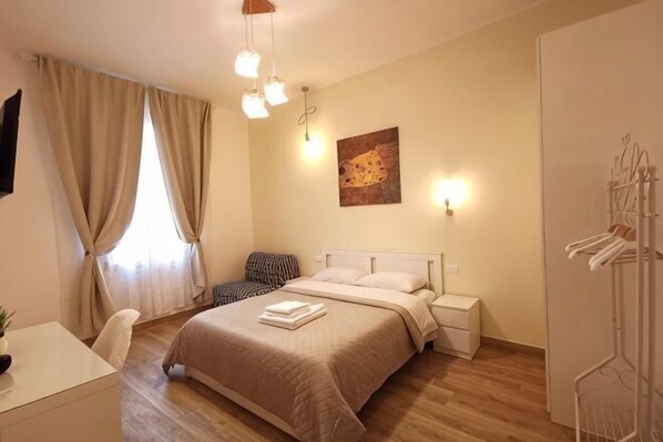 A bedroom with a bed, bedside tables, a chair, a desk, a wardrobe, and a hanging rack. - Casa di Serena (Venice)