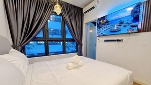 A hotel room with a bed, a TV on the wall, and a window with curtains.