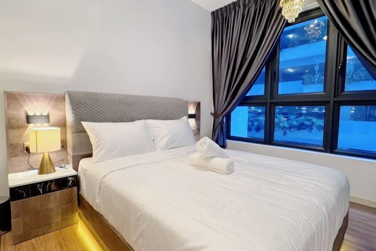 A hotel room with a bed, a nightstand with a lamp, a window with curtains, and a view of the outside.