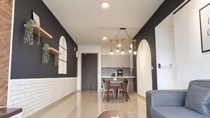 A modern living room with a sofa, a coffee table with a box, a kitchen area with a dining table and chairs, and a hallway with a door.