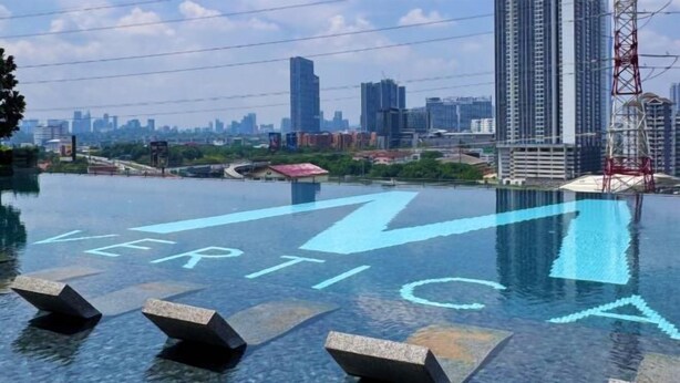 An infinity pool with the word "VERTICAL" and directional arrows on the floor, surrounded by high-rise buildings.