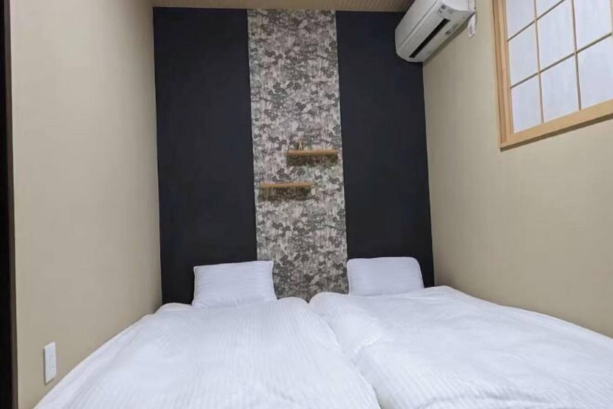 A bedroom with a bed, a wall-mounted air conditioner, and a window with a grid pattern.