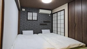 A bedroom with a bed, a wall-mounted air conditioner, a window with a grid pattern, and a wooden wardrobe. - Moonlight Inn Kujo (Kyoto)