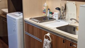 A compact kitchen with a built-in washing machine, a sink, and a dish rack. - Moonlight Inn Kujo (Kyoto)