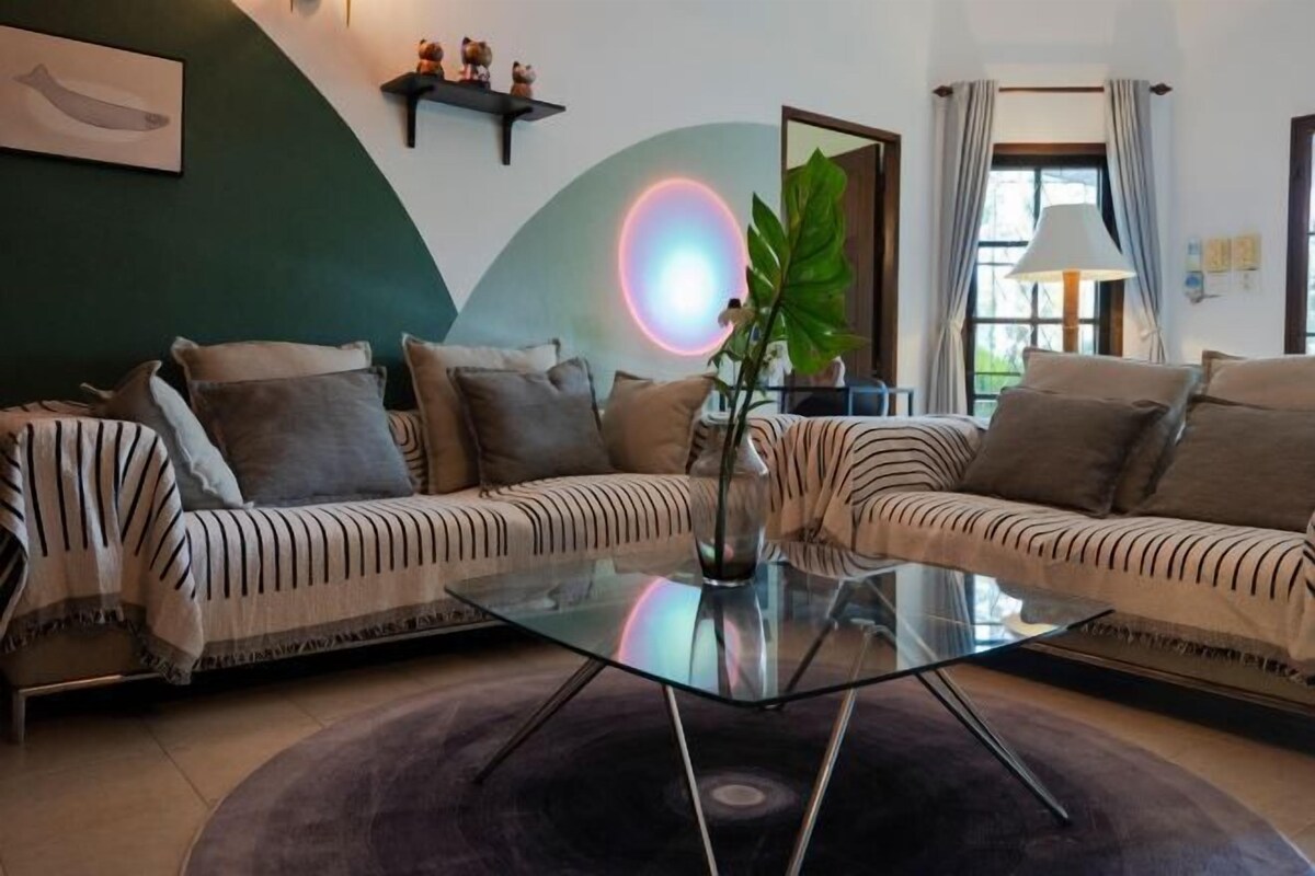A modern living room with a sectional sofa, a glass coffee table, and a large plant.