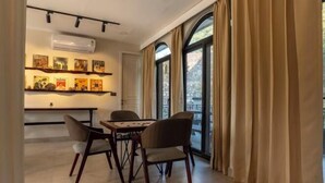 A dining area with a table and chairs, a wall-mounted air conditioner, and a window with curtains. - Chakk 109 Mussoorie Foothills, Dehradun (Dehradun)