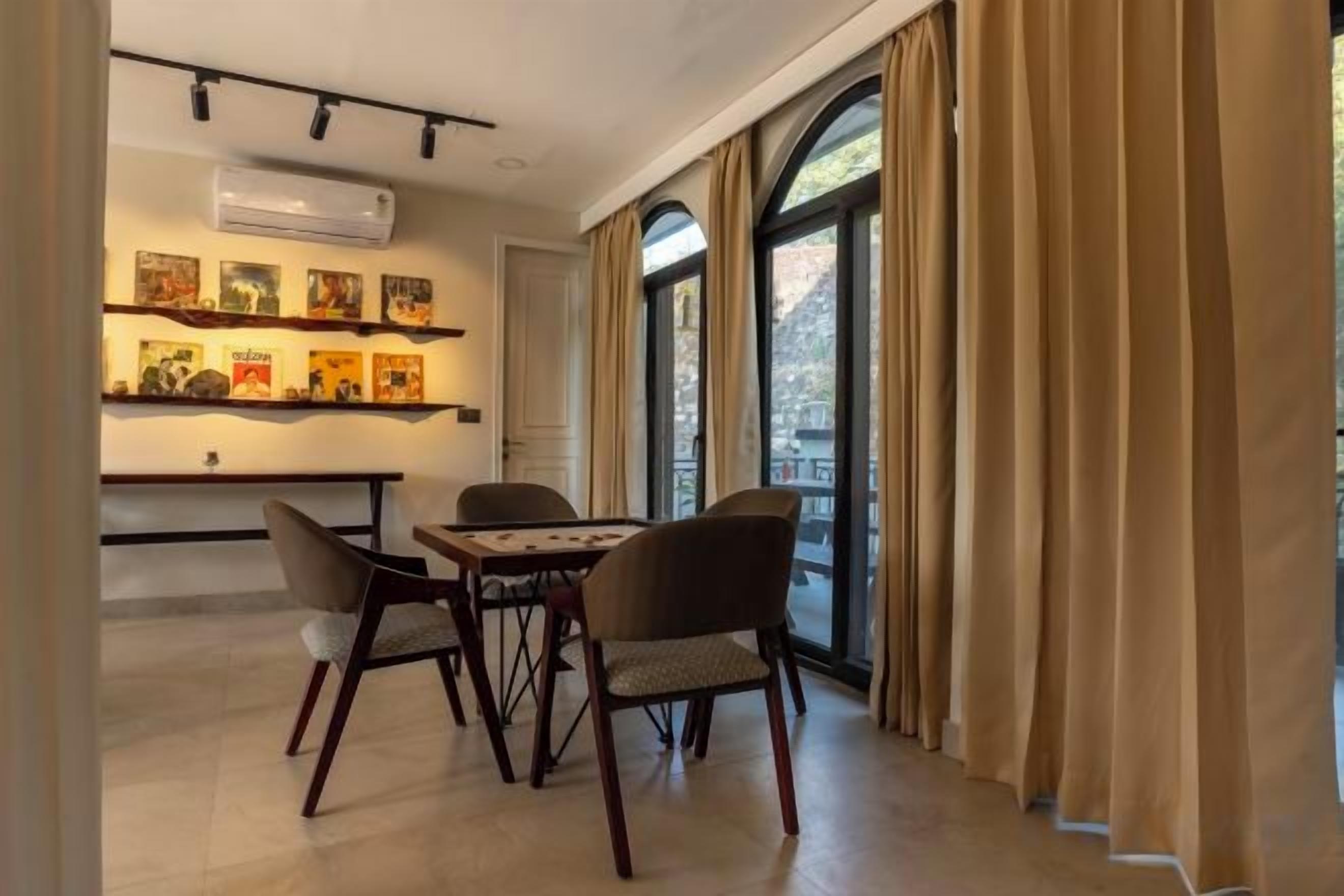 A dining area with a table and chairs, a wall-mounted air conditioner, and a window with curtains.