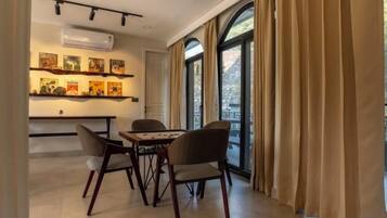A dining area with a table and chairs, a wall-mounted air conditioner, and a window with curtains.