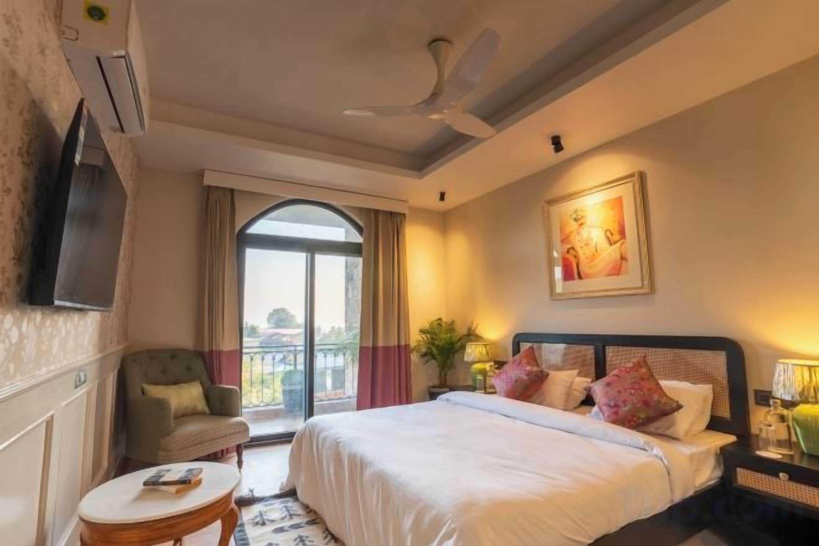 Une chambre d’hôtel avec un lit, une chaise, une petite table, une télévision et un balcon.