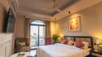 Habitación de hotel con cama, una silla, una mesita, televisor y balcón.