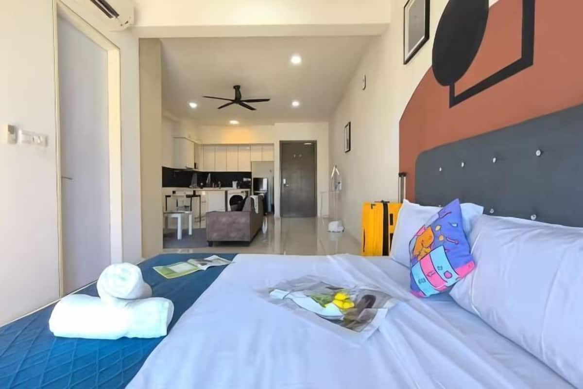 Ein Hotelzimmer mit einem Bett, einem Kissen, einem gefalteten Handtuch, einer Zeitschrift und Blick in die Küchenzeile.
