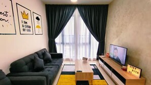 Un salon moderne avec un canapé, une table basse, un téléviseur et un panneau indiquant : « RESTEZ AVEC NOUS ».