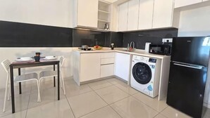 Une cuisine compacte équipée d’un lave-linge, d’un réfrigérateur et d’un coin repas avec des chaises.