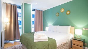 A hotel room with a bed, a nightstand, a lamp, and a view of the outdoors. - Thesqua.re Saffron Hill Apartments (London)