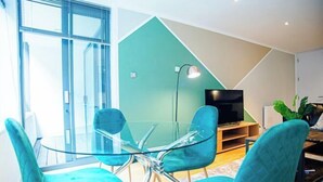 A modern living room with a glass dining table, teal chairs, a flat-screen TV, and a green accent wall. - Thesqua.re Saffron Hill Apartments (London)
