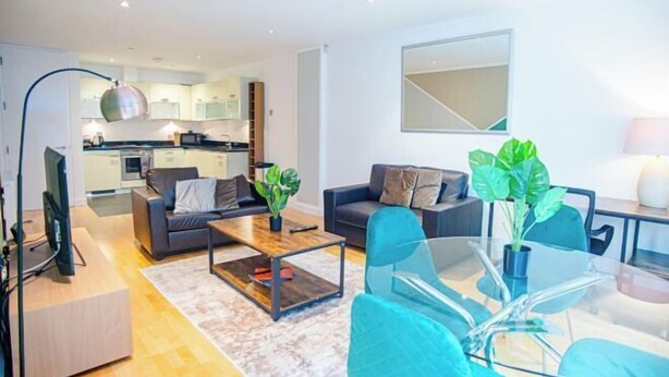 A modern living room with a sofa, coffee table, and glass dining table. There is a kitchen in the background with cabinets and a microwave. - Thesqua.re Saffron Hill Apartments (London)