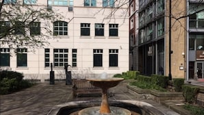 A courtyard with a fountain, a bench, and a building with large windows. - Thesqua.re Saffron Hill Apartments (London)