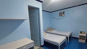 A small, single-room accommodation with a desk, two single beds, a door, and a small shelf. - Green Mellow Court Capitol Avenue (Dipolog)